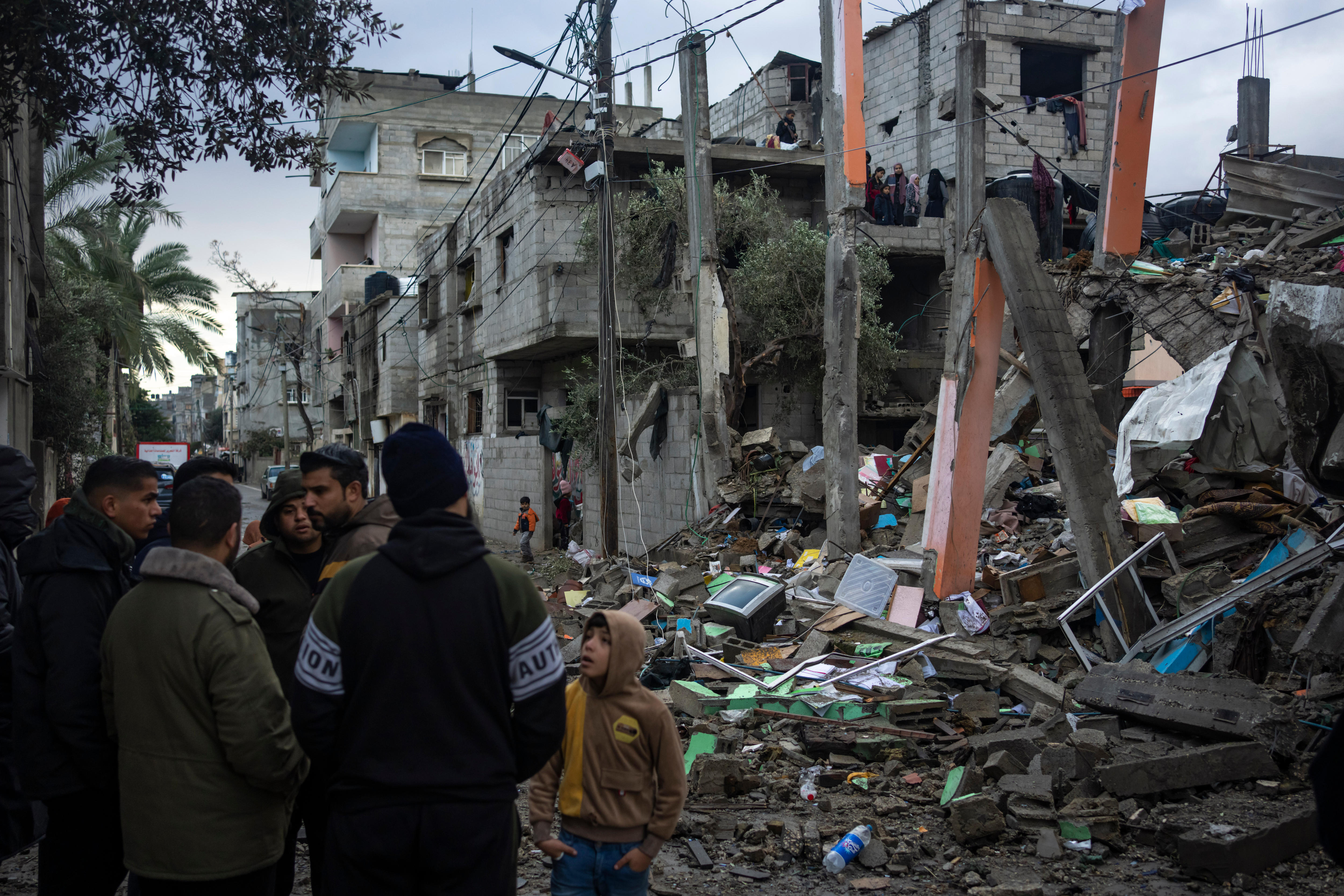 A group of people stand in front of a destroyed building. 