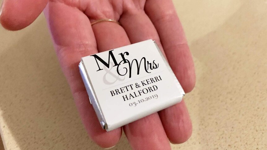 A hand holds a packet with wedding chocolates. Th wrapping says Mr and Mrs Brett and Kerri Halford. 3 October, 2019.