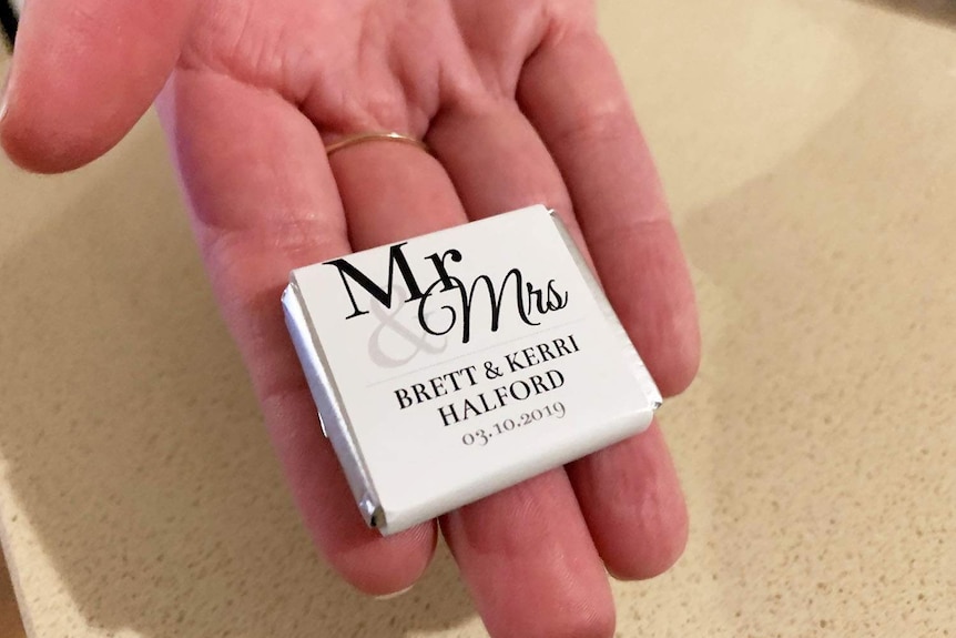 A hand holds a packet with wedding chocolates. Th wrapping says Mr and Mrs Brett and Kerri Halford. 3 October, 2019.
