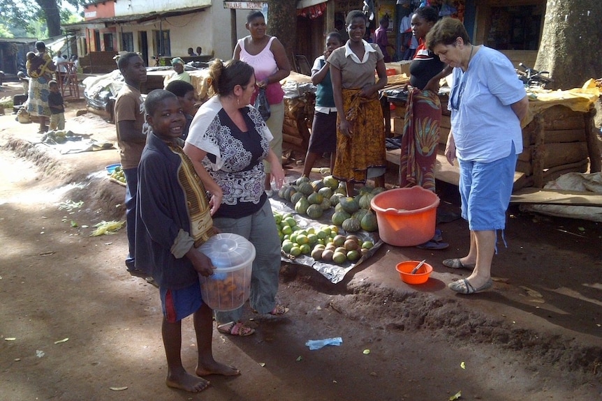 Two middle-aged white women in a marketplace with several African children