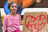 Viktoria Veisbrut stands in front of a wall that says peace and love in bubble writing. 