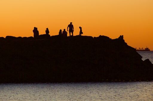 Sunset at Cottesloe beach with silhouettes of people standing on rocks.