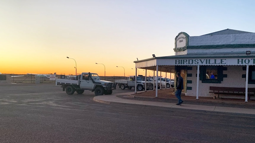 Sunset shimmers in distance at the Birdsville Hotel with four-wheel-drive vehicles parked in front.