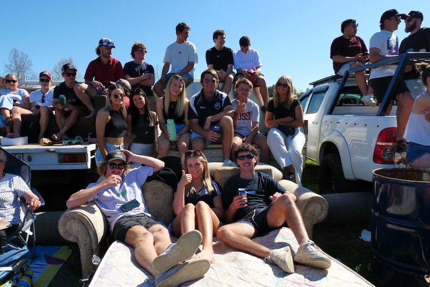 People watch the football sitting on their cars and a sleeper sofa