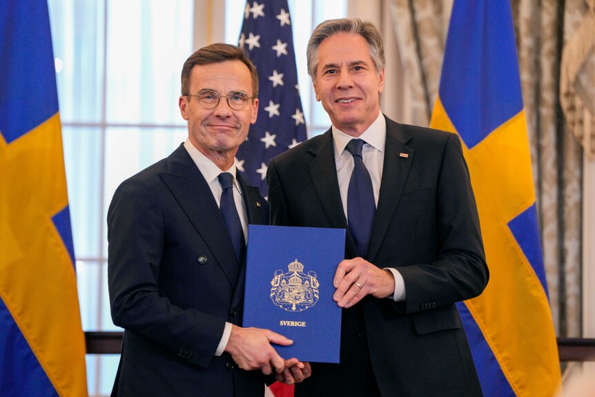 Ulf Kristersoon poses for a photo with Antony Blinken. They are standing in between two Swedish flags.