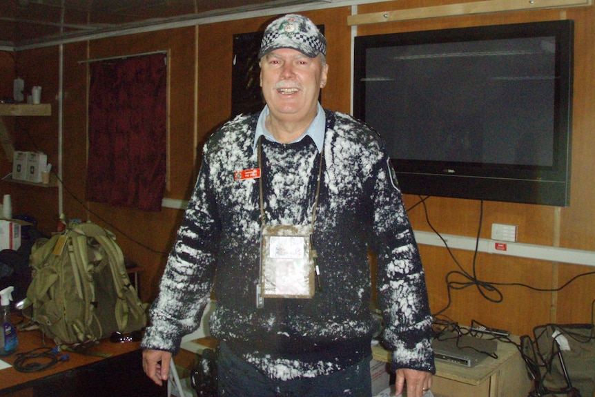 A man in an AFP uniform covered in snow stands inside an office, smiling