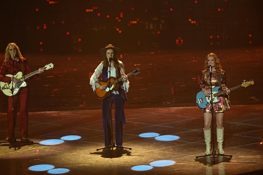 Trois femmes ont de petits drapeaux ukrainiens faits de ruban adhésif sur leurs guitares et leurs mains.