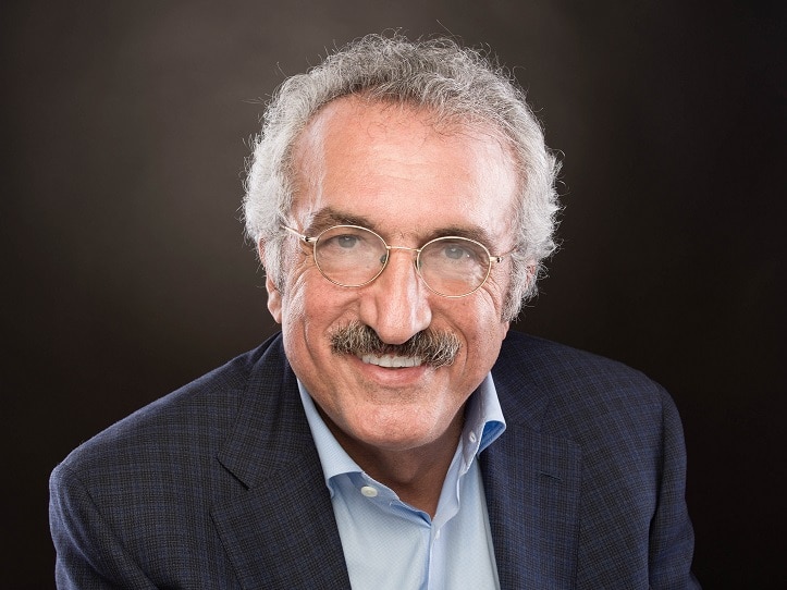 Professor Abbas Milani is wearing glasses and smiling, in a navy suit and blue shirt.