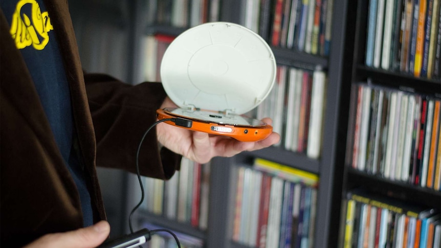 A hand holds a walkman in front of a collection of CDs
