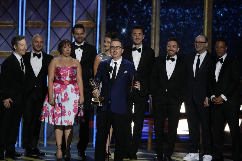 John Oliver stands in front of his team holding the Emmy trophy