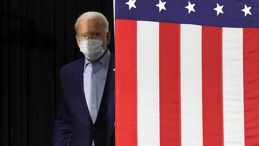 Democratic US presidential nominee and former Vice President Joe Biden steps out from behind an American flag