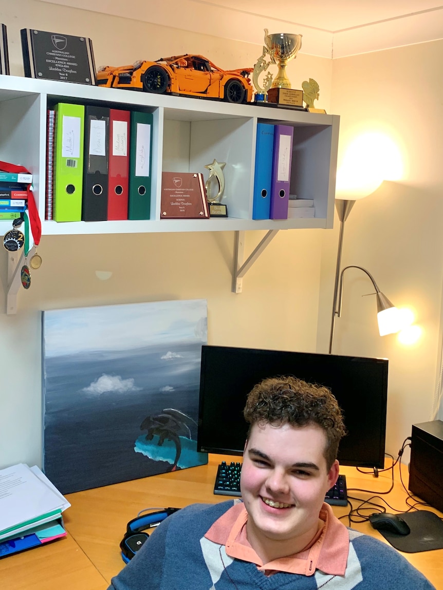 A student in his home learning set up with his back to a computer screen and desk and bookshelf above