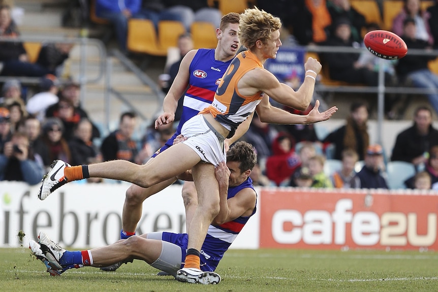 A footballer tries to handball the ball away while being tackled.