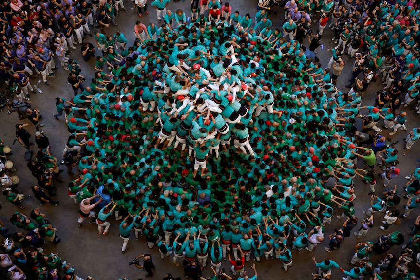 A large pile of people in teal shirts, some forming a large circle, others collapsed on top of each other in the middle.