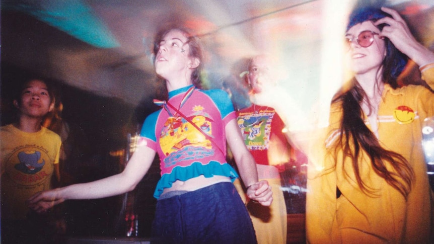 Young people in bright clothes dance in a dark room