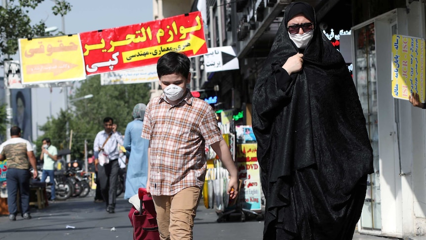 An Iranian woman, clad in an abaya and a protective face mask, walk with her son, who is also wearing a mask,  in the street.