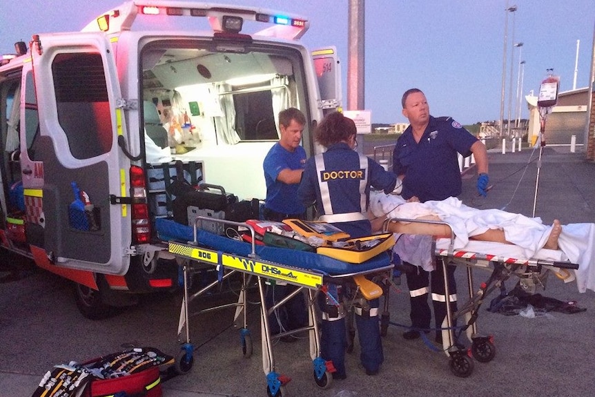 Patient lying on stretcher, being treated by paramedics next to a ambulance.