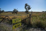 A yellow sign on a metal gate reads 'stop Bowdens mine' in a rural landscape