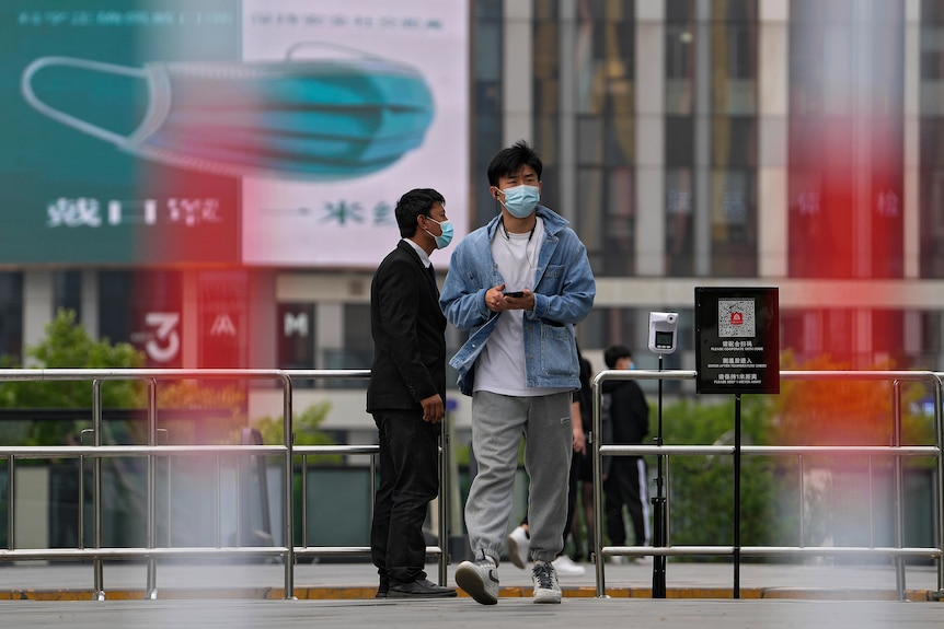 A man wearing a face mask walks by a masked security stands guard at a barricaded entrance.