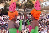 Two drag queens dressed in matching watermelon themed costumes entertain a large crowd outdoors.