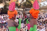 Two drag queens dressed in matching watermelon themed costumes entertaina large crowd outdoors.