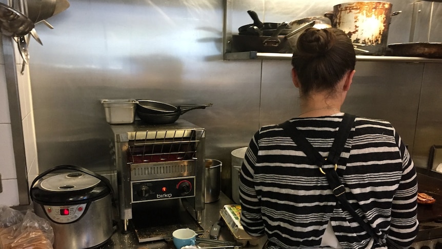 Young woman stands in cafe kitchen preparing food.