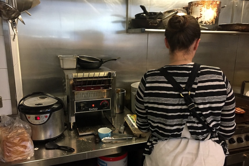 Young woman stands in cafe kitchen preparing food.