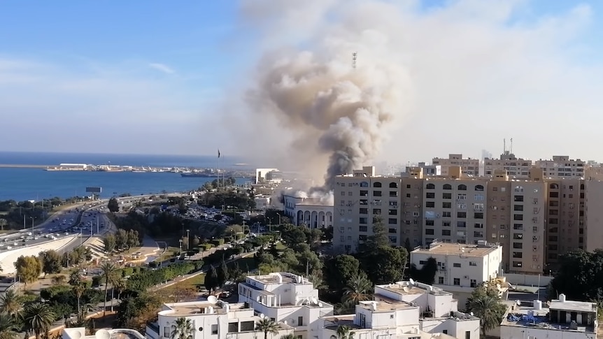 The Libyan Foreign Ministry is up in smoke as seen from a high elevation within Tripoli, with the sea to the left side.