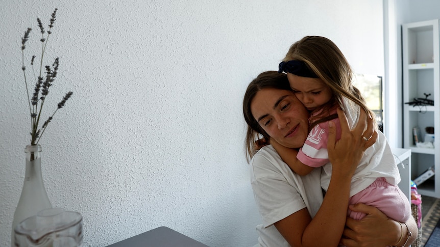 A young girl clings onto her mother as they hug. 