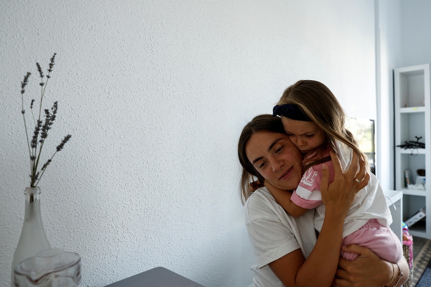 A young girl clings onto her mother as they hug. 