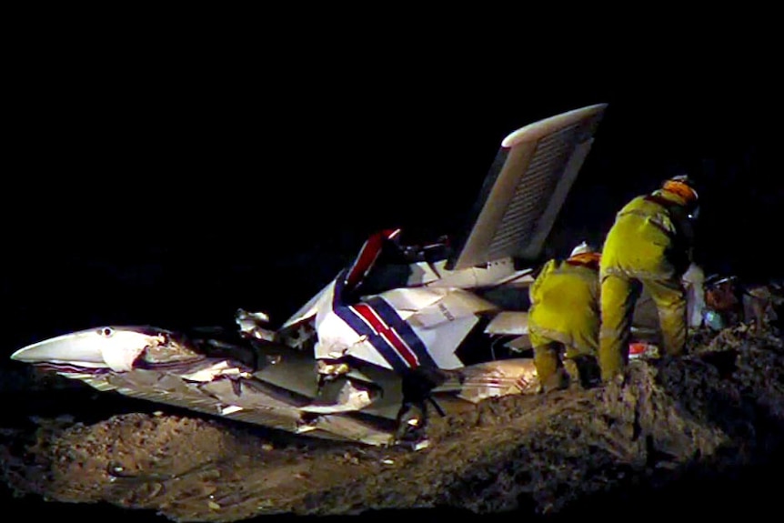 Emergency services officers look at the wreck of a light plane after it crashed near Cable Beach.