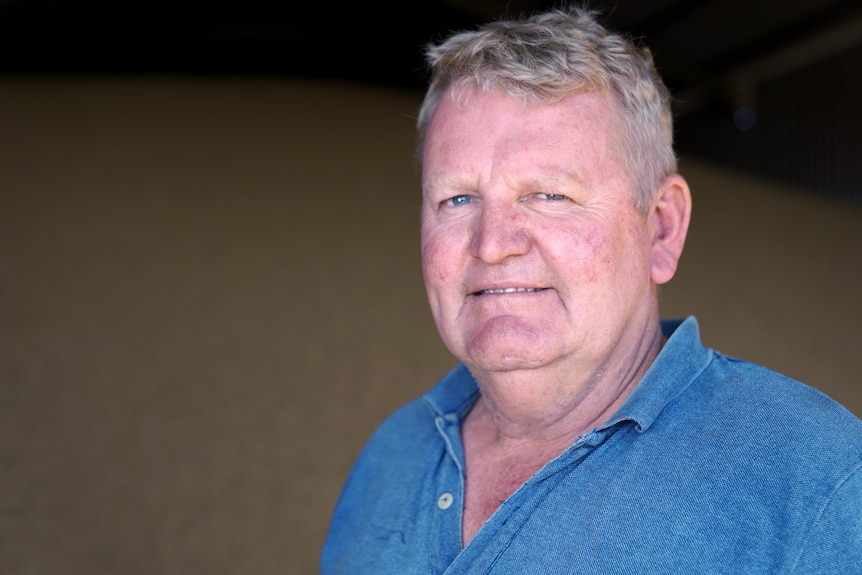 A middle-aged farmer in a grain shed, wearing a blue shirt