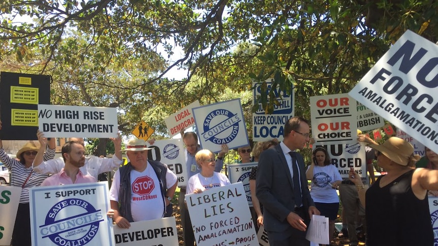 Protesters hold signs with slogans opposing council amalgamations.