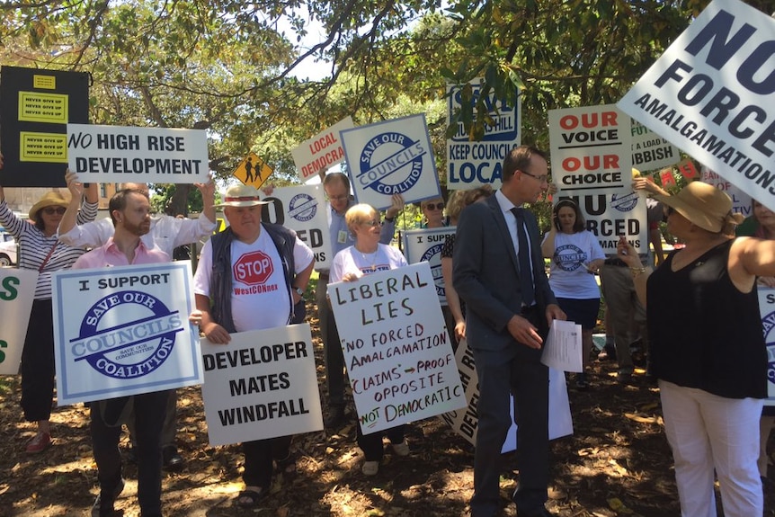 Protesters hold signs with slogans opposing council amalgamations.