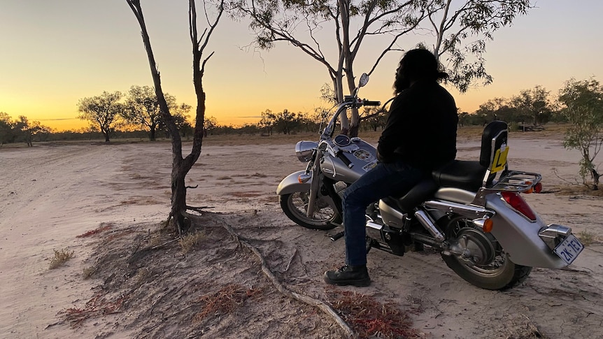 A silhouette of a man on a motorbike with a sunset in the background.