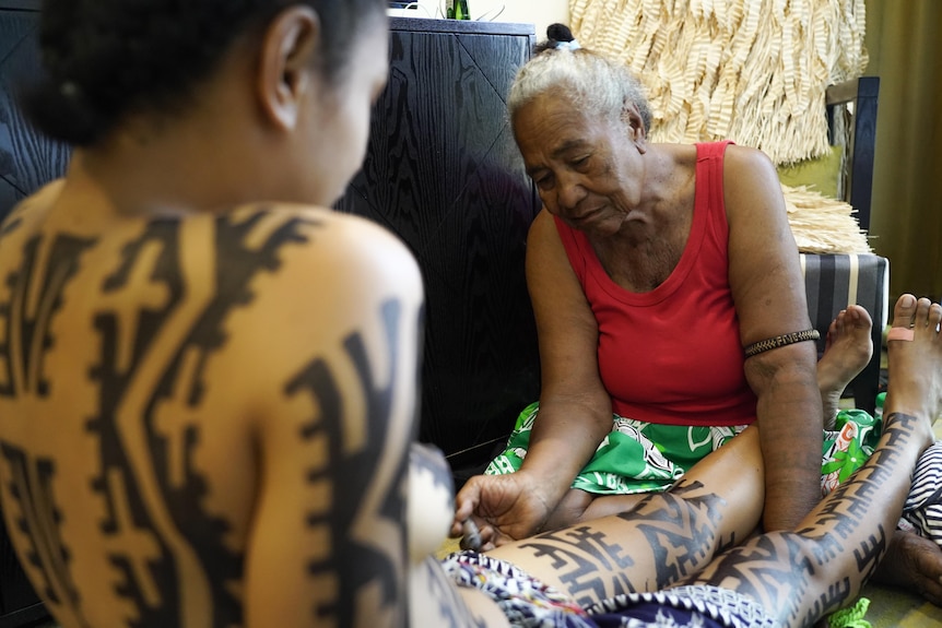 Great-grandmother drawing tattoos on a young woman.