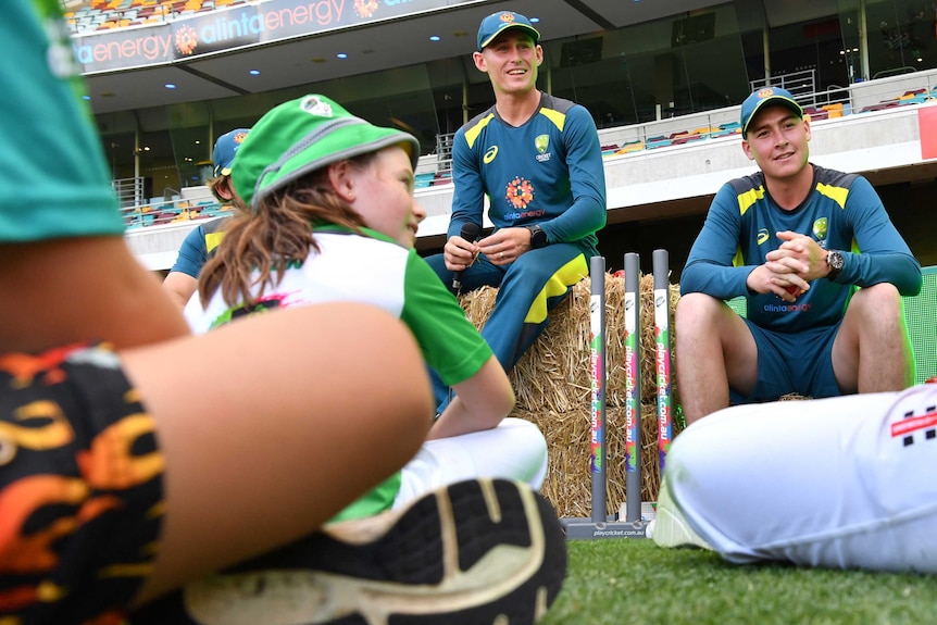 Two male Australian cricketers speak to children at a junior coaching clinic at the Gabba in Brisbane.