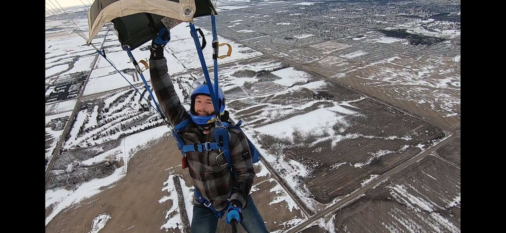A man in a parachute above a snowy field