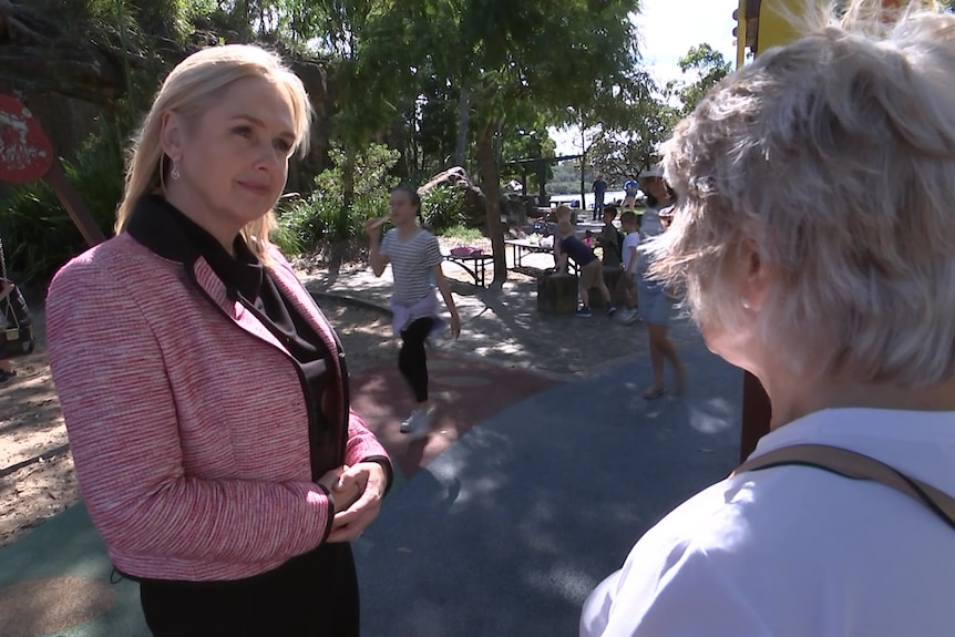 A serious looking woman speaks to an older woman in a children's playground