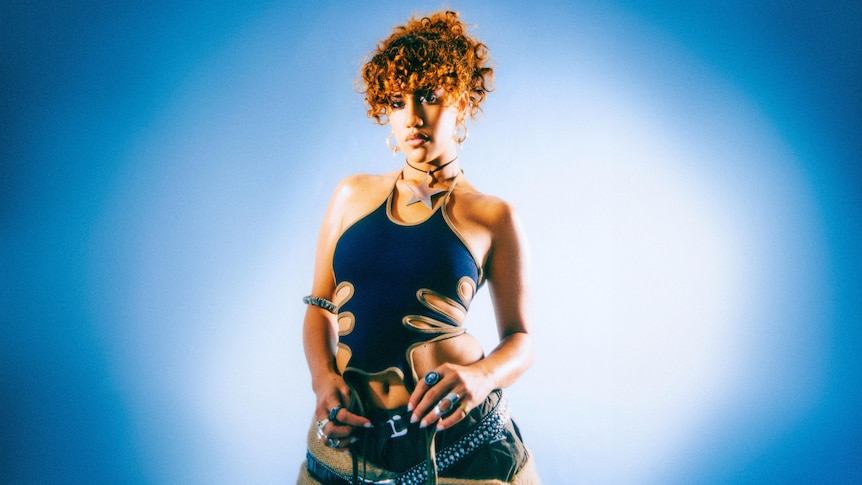A portrait og Becca Hatch in a cutout blue bodysuit and a denim skirt with her curly hair pulled back