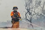 A fireman with a big white beard and sunnies holding a hose