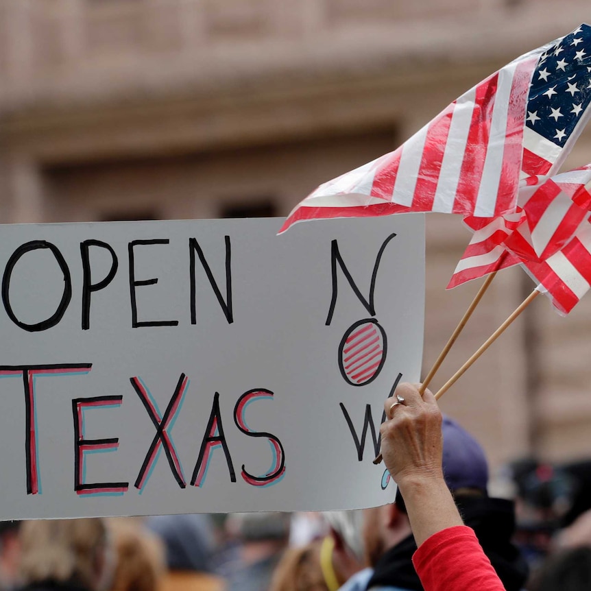 US flag and sign reading "open Texas now" at a protest in Austin, Texas.