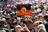 A person in a crowd holds up a sign with the Aboriginal flag and the words "Voice to Parliament". 