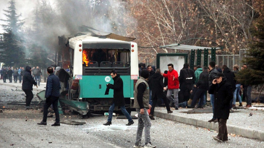 A public bus is burning at the scene of a car bomb attack