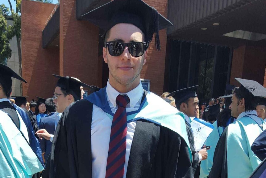 A young man in dark glasses dressed in graduate's garb.