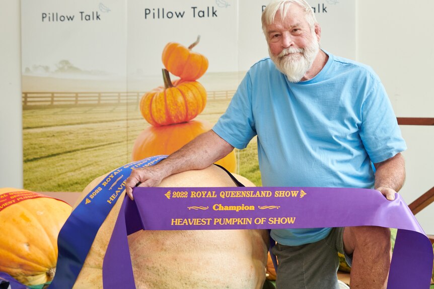 White haired man next to giant pumpkin holding ribbon.