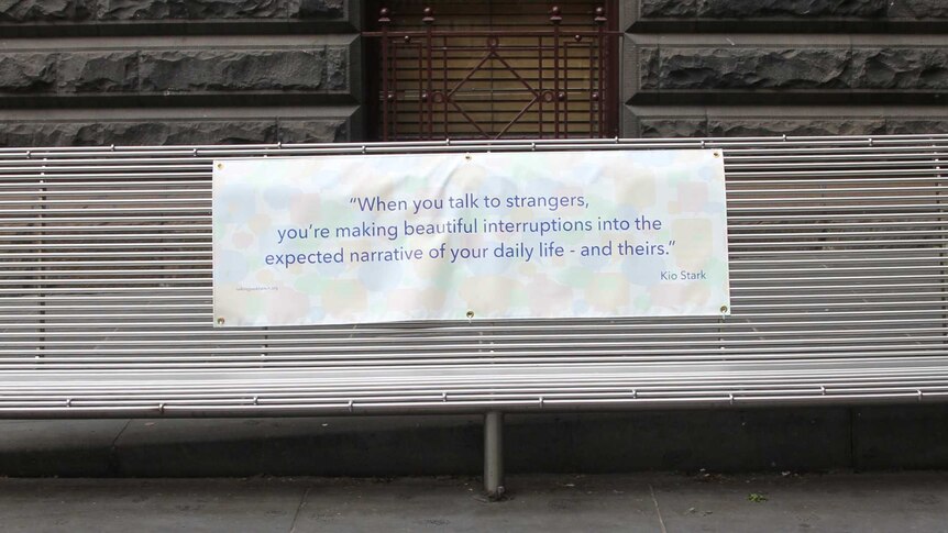 A famous quote about speaking to strangers written on a banner is placed on a park bench.