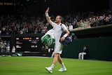Tennis player Andy Murray carries bags on either shoulder as he raises his right hand in acknowledgement to the Wimbledon crowd.