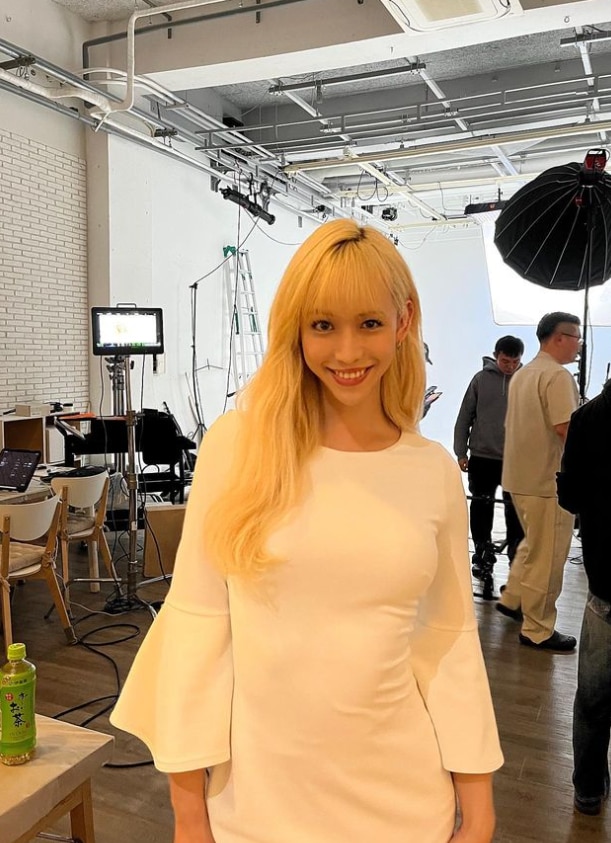 A blonde Japanese person smiles into the camera at a film set. 
