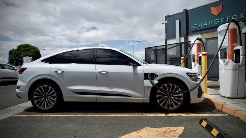 A sporty-looking car is parked in front of an electric charging station, connected to a charger.